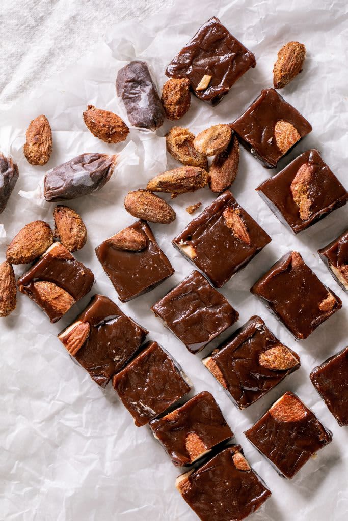 Homemade toffee salted caramel chocolate almond nuts candy on crumpled paper in row over white linen tablecloth. Handmade food sweet gifts for any holidays. Flat lay. (Photo by: Natasha Breen/REDA&CO/Universal Images Group via Getty Images)