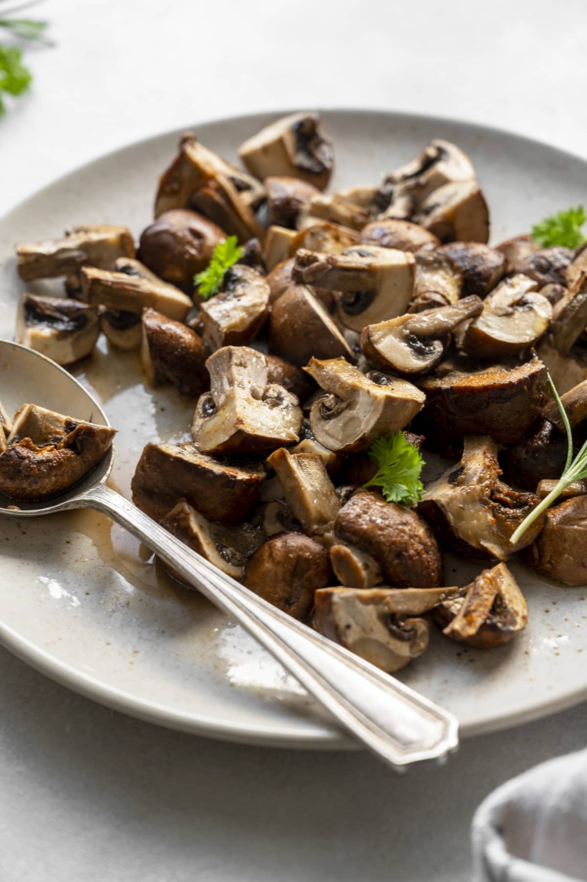 Roasted mushrooms on a white plate with herbs and a silver spoon