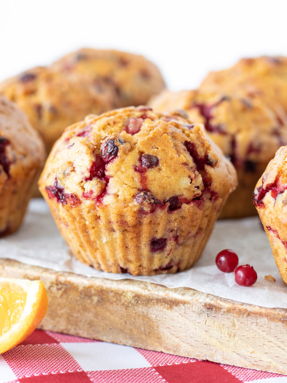 Cranberry orange muffin on a wooden table with white background. Vertical shot, a closeup. Freshly baked vegan muffins with cranberries and orange juice. Sweet vegan breakfast, dessert, or snack.