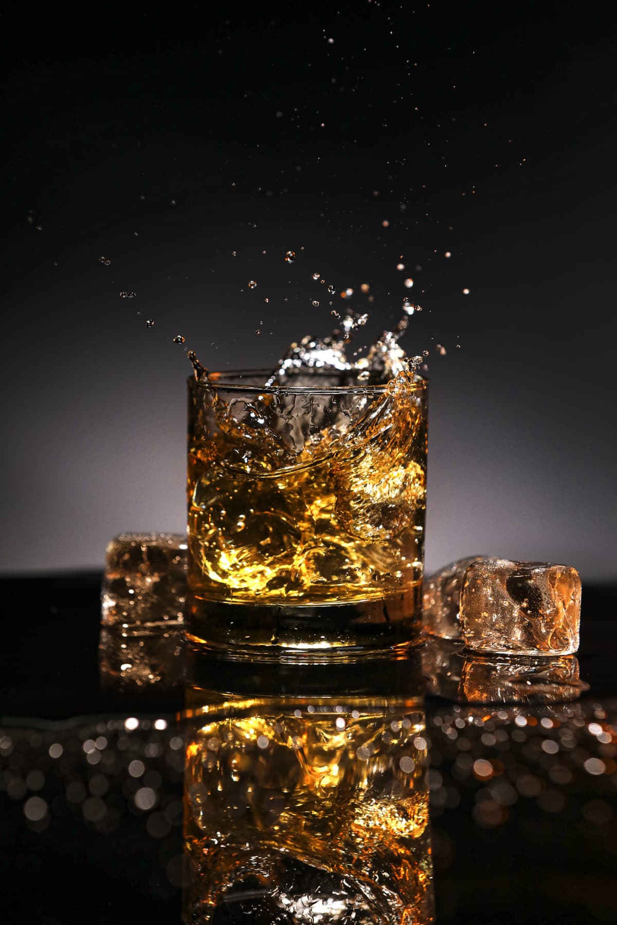 A glass of whisky with ice spilling on a dark background.