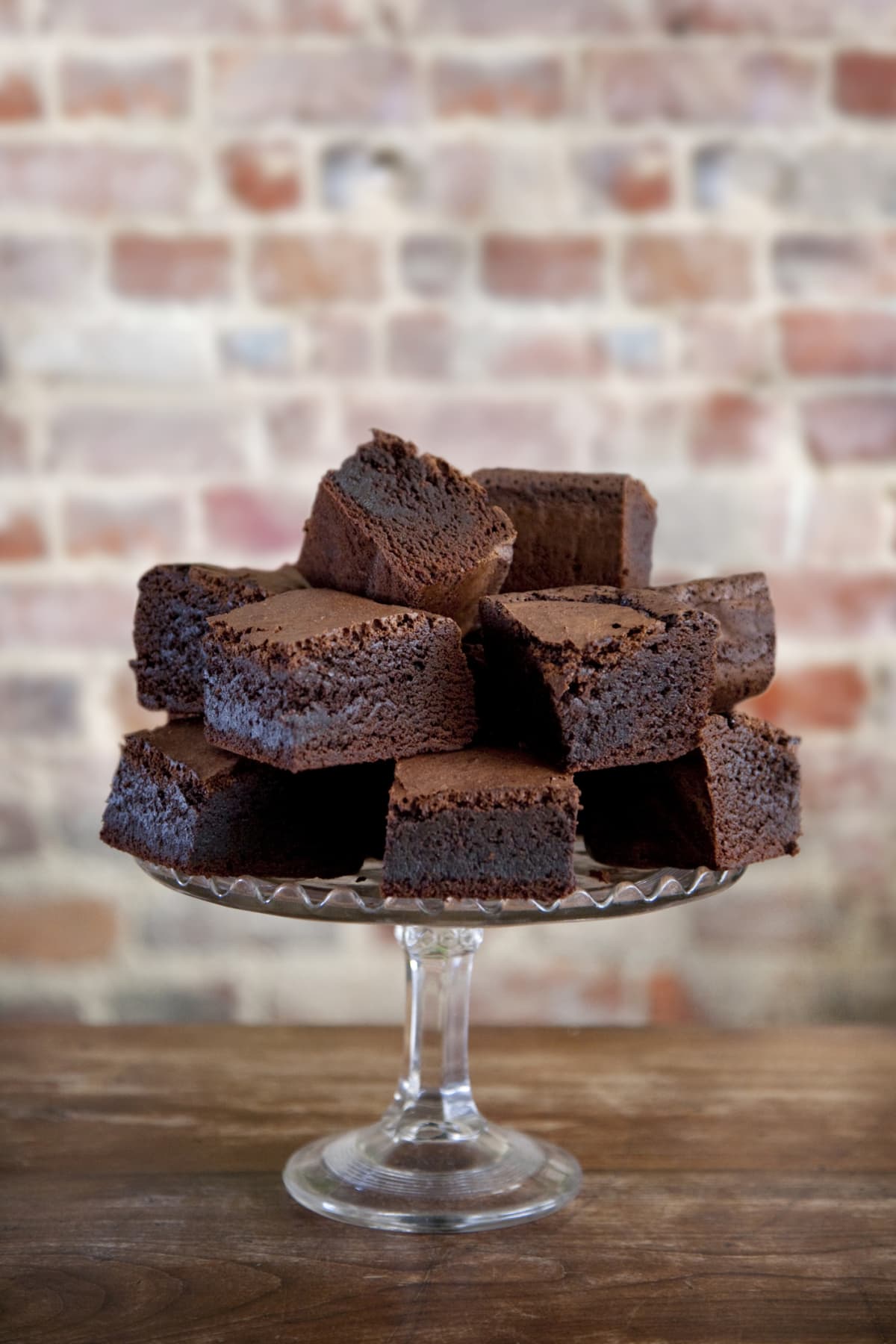 Several sliced brownies piled on top of a glass cake stand