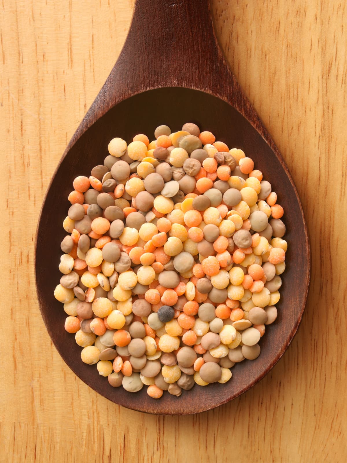 Top view of wooden spoon with mix of raw lentils on it