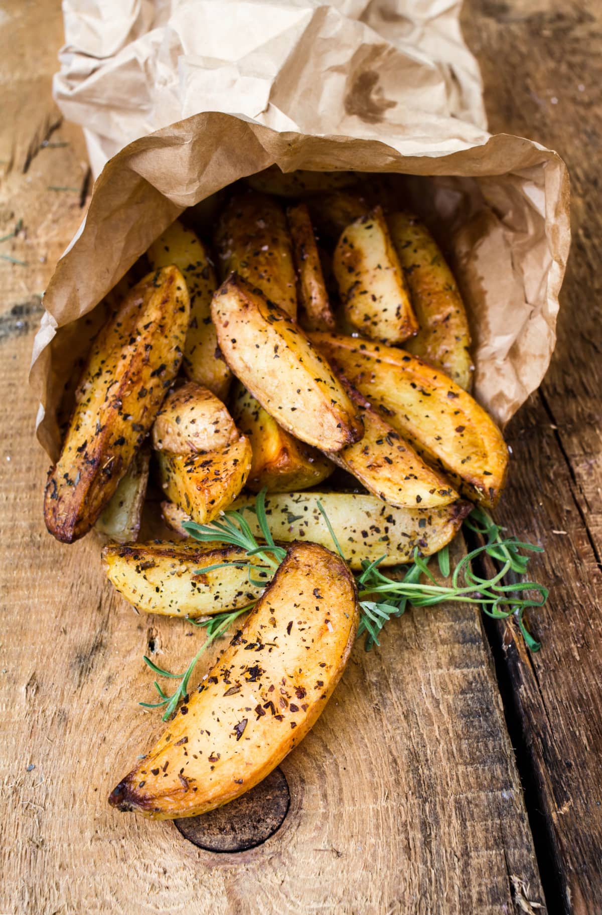 French fries potato wedges in recycled kraft paper bag on wooden old background