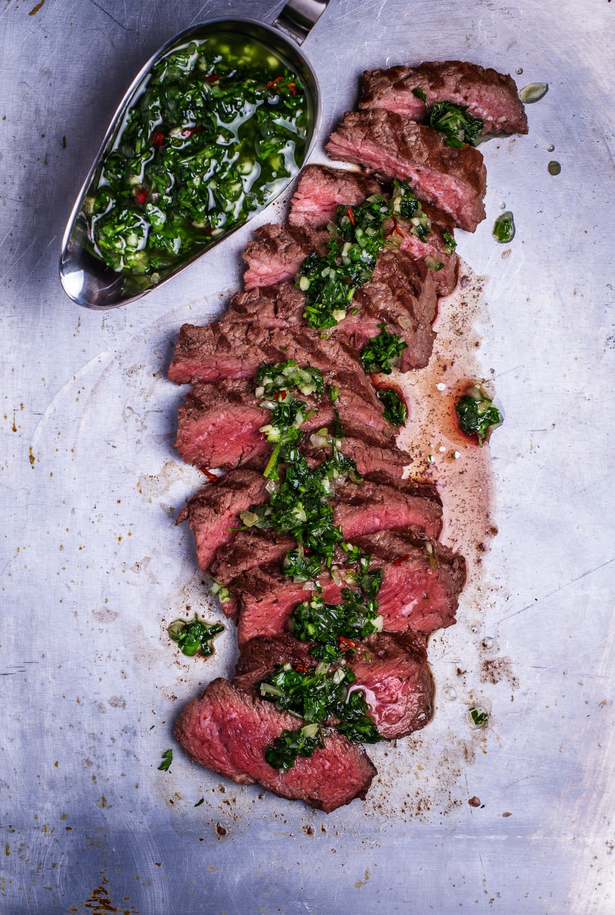 Graavy boat of chimichurri sauce next to skirt steak sliced and topped with chimichurri