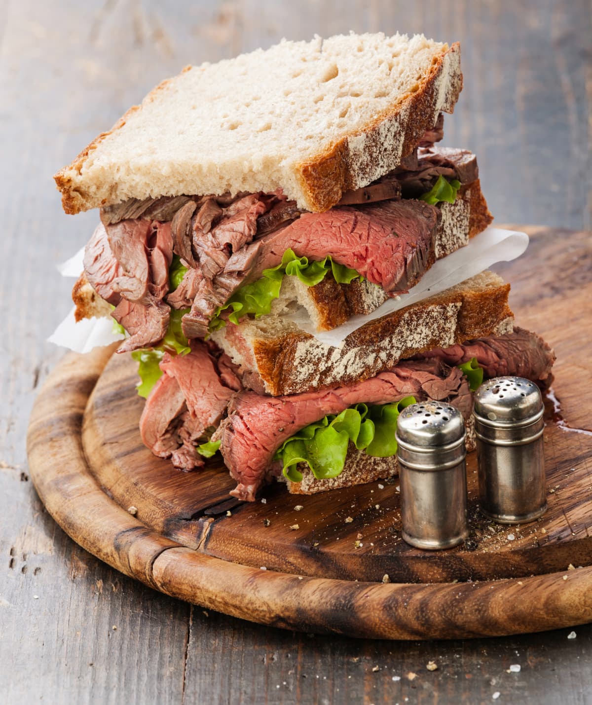 Roast beef sandwiches with lettuce on wooden cutting board on dark wooden background
