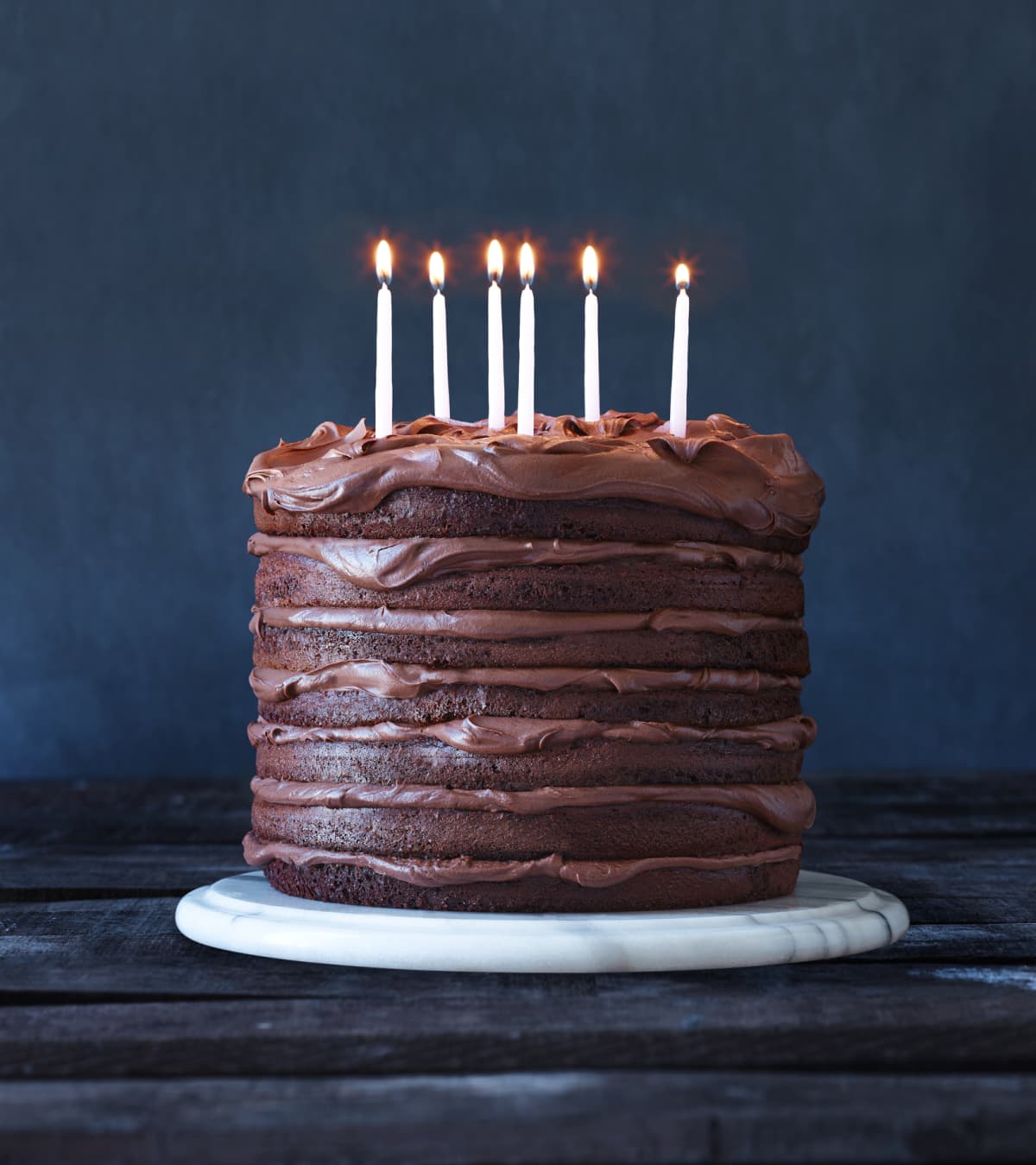 A large layered chocolate birthday cake with 6 lit candles.