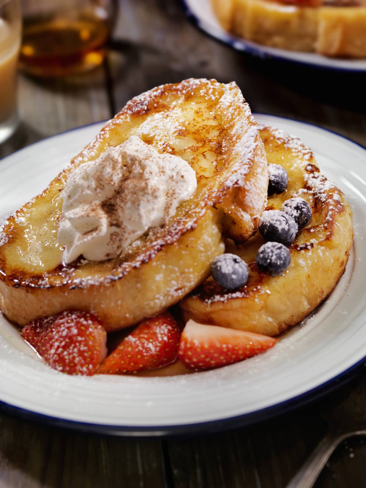 Two slices of French toast on plate with powdered sugar, fruit, and whipped cream