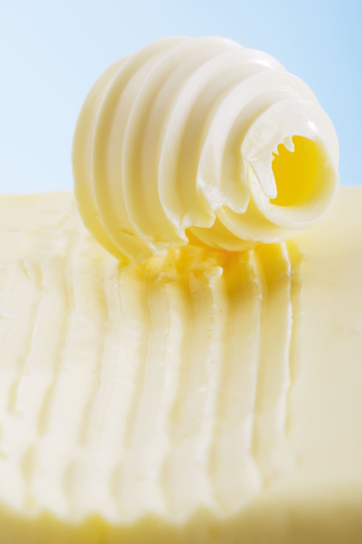 Stick of organic butter melting on white surface with shadow.