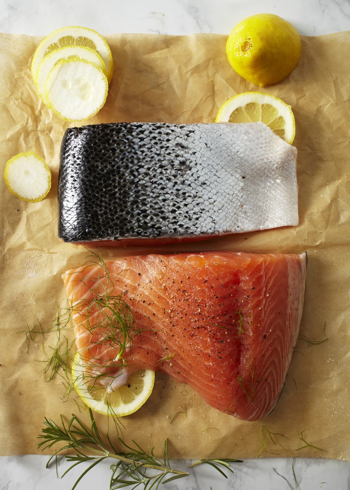 Whole raw uncooked salmon fillet server with green dill, lemon, salt, pepper, chefs knife over dark brown texture background Top view, space. (Photo by: Natasha Breen/REDA&CO/Universal Images Group via Getty Images)