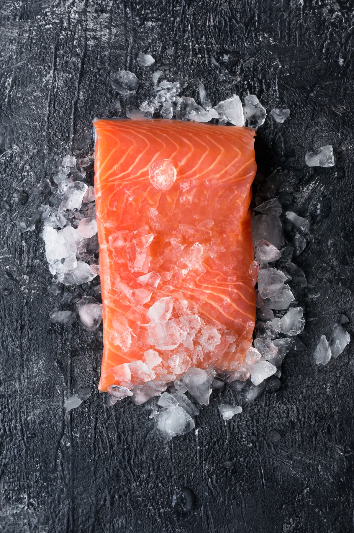 Raw salmon filet on a black surface with crushed ice