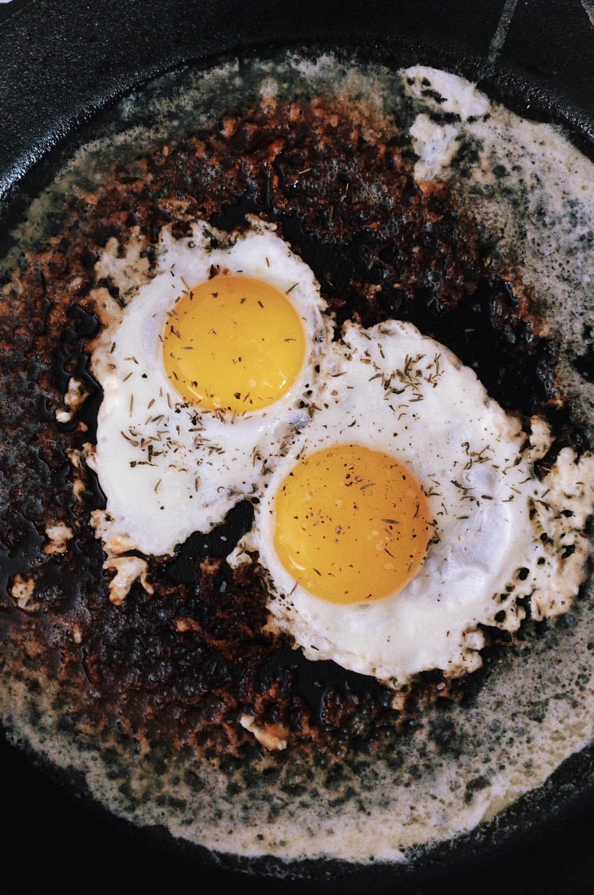 Two eggs cooked in a cast-iron skillet on top of parmesan cheese. Mobile photo. Processed with VSCO with k3 preset