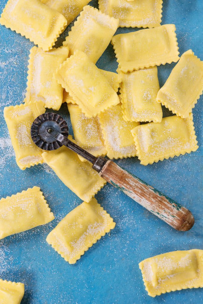 Fresh maked raw uncooked italian pasta ravioli with flour and vintage pasta cutter over bright blue wooden background. Top view with copy space. (Photo by: Natasha Breen/REDA&CO/Universal Images Group via Getty Images)