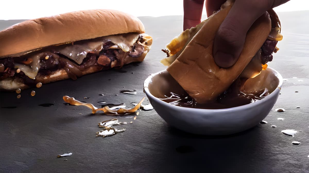 Hand dipping a French dip sandwich into jus