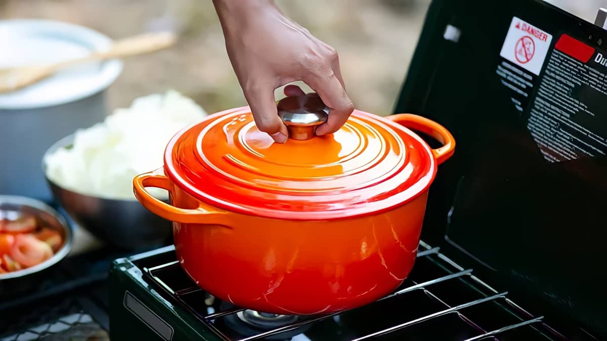 Hand removing the lid from an orange Dutch oven