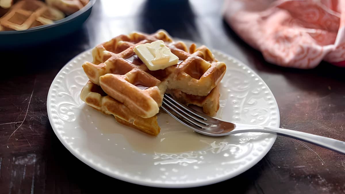 Stack of waffles with syrup and butter on a white plate with a fork
