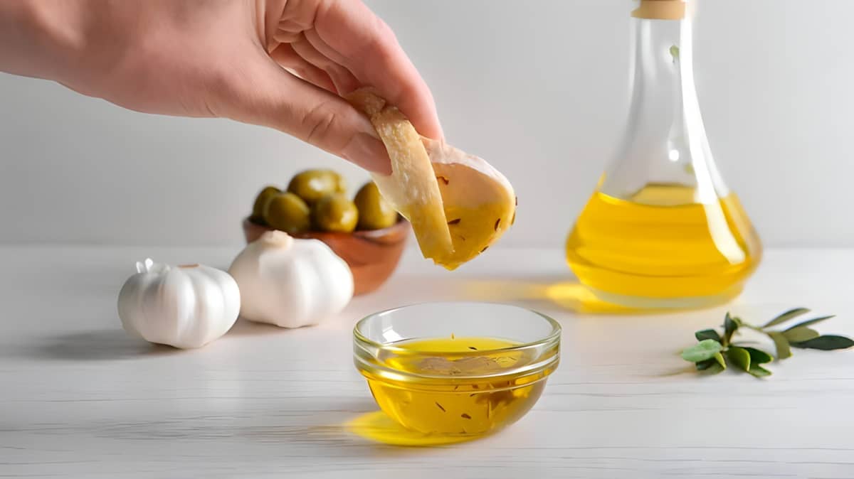 A woman dips a bread slice into a seasoned olive oil