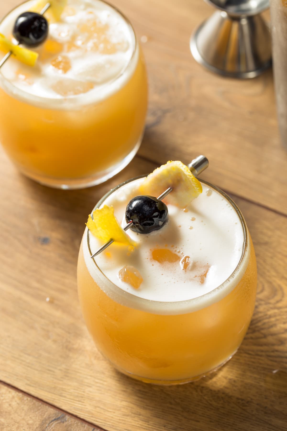 Whiskey sour in glass with lemon peel and cherry garnish