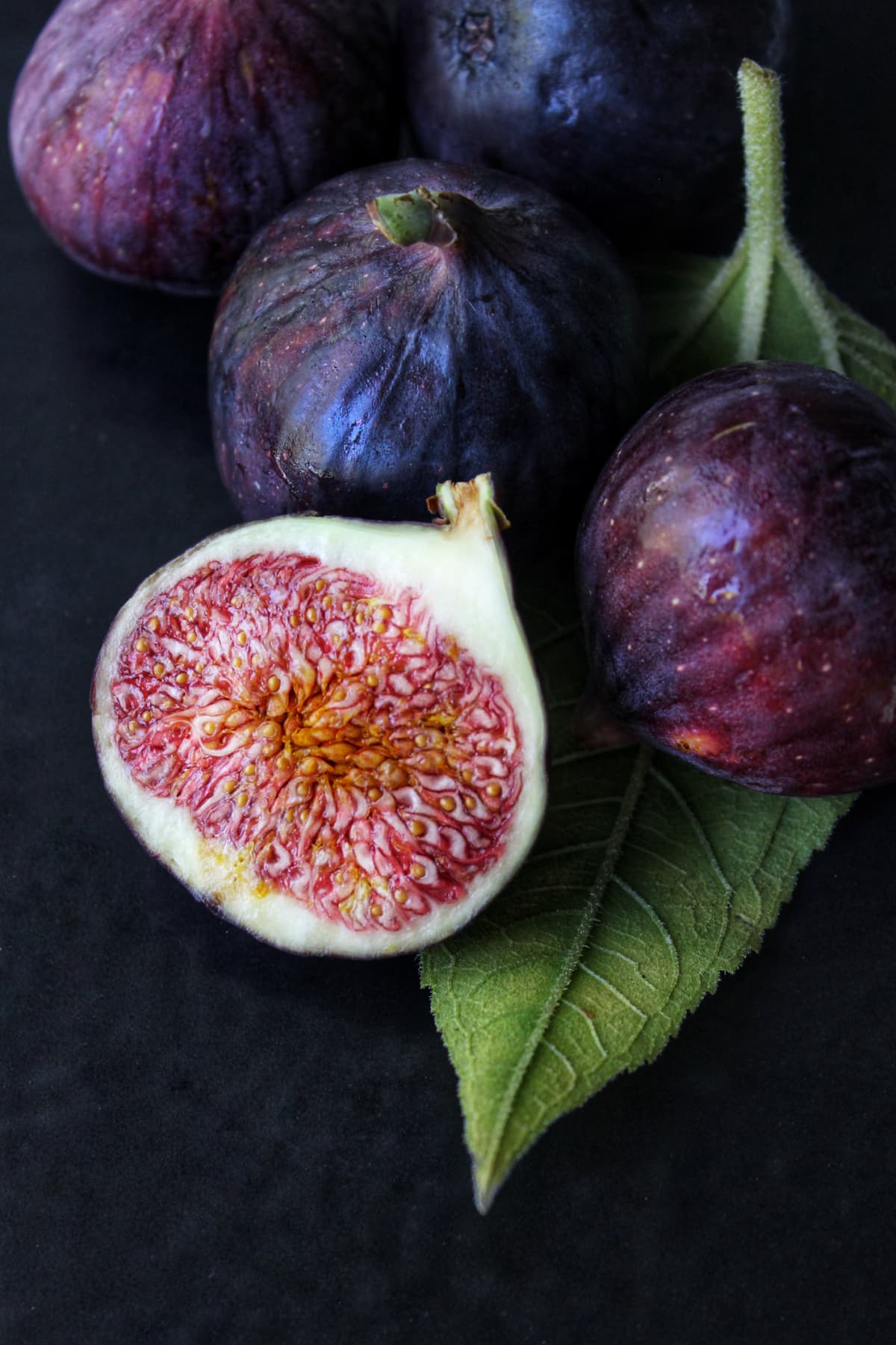 A slice of ripe figs with a green leaf on a dark background close-up.Texture or background