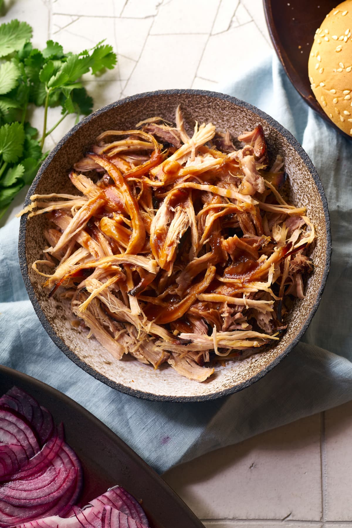 Bowl of shredded pork with onion and cilantro on the side