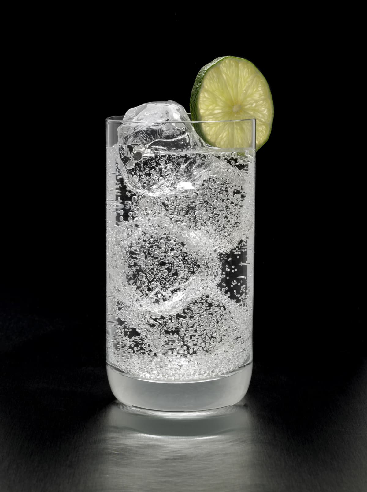 A refreshing gin, vodka or rum and tonic cocktail with a lime garnish, shot against a black background.