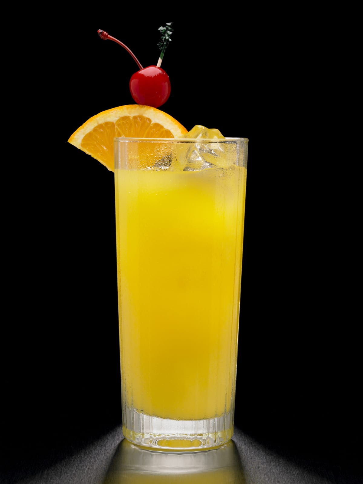 A screwdriver, or Vodka and orange juice cocktail, shot on a black background and garnished with an orange and a cherry.
