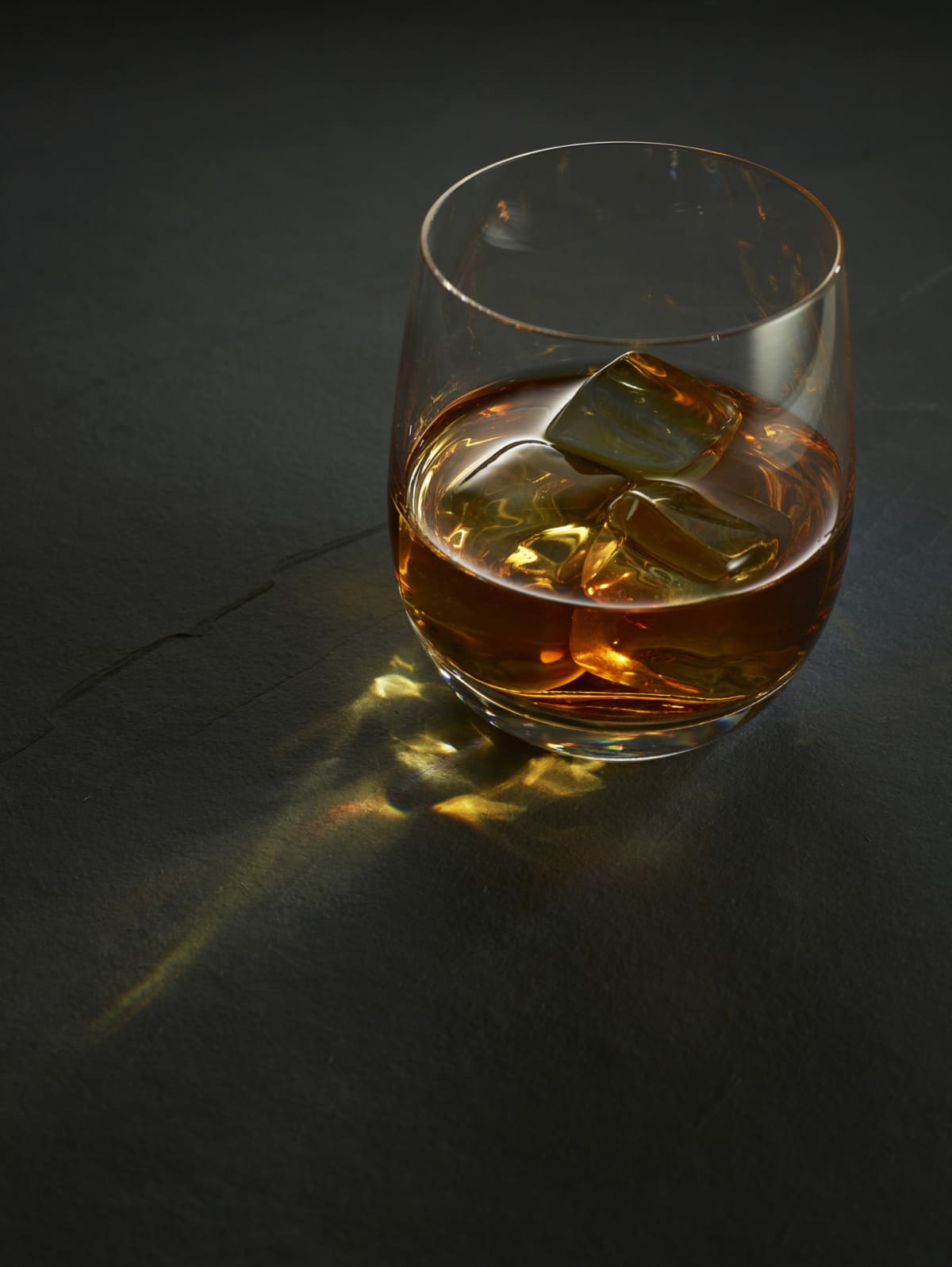A glass of whiskey on the rocks on a slate table top