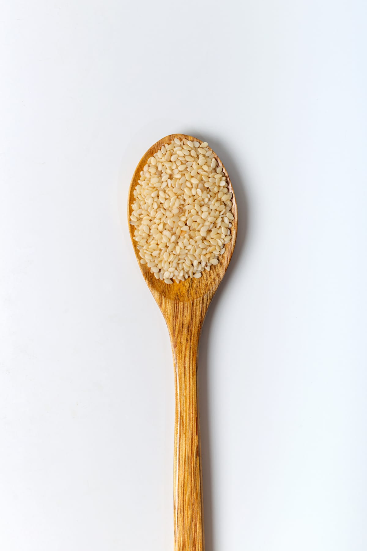 Sesame seeds in a wooden spoon isolated on white background