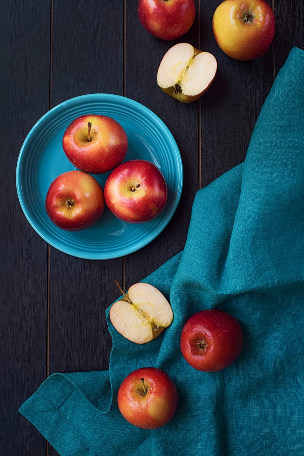 Composition of fresh apples on a blue plate and a blue napkin on a black wooden table
