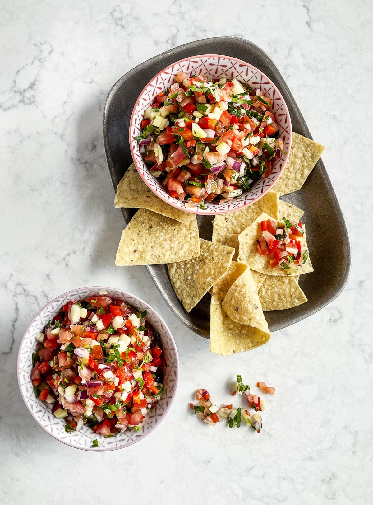 Salsa in bowls with tortilla chips around them on a tray and white surface