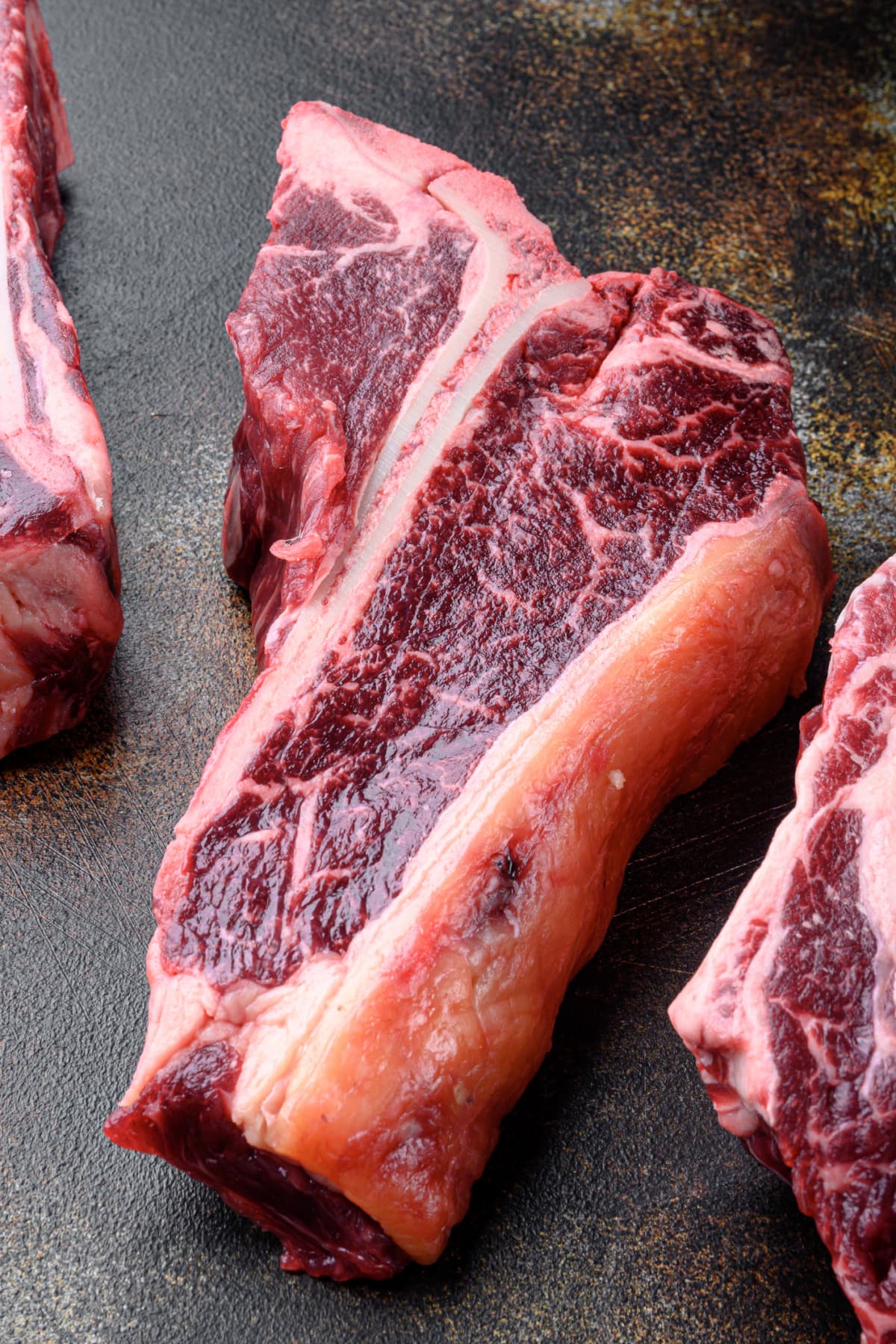 Dry-aged raw T-bone or porterhouse beef steak set on old dark rustic background