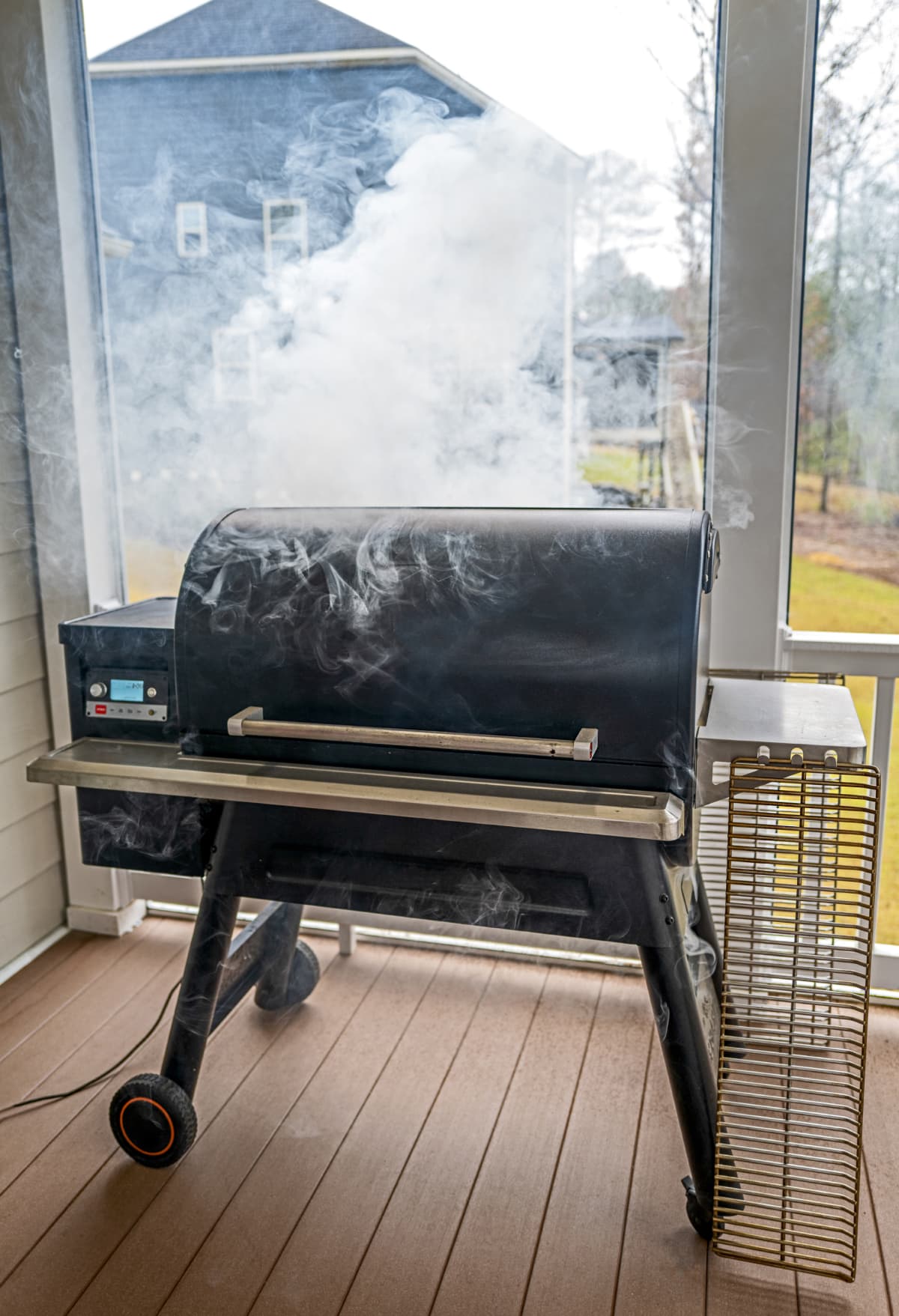 A BBQ smoker on a porch giving off smoke