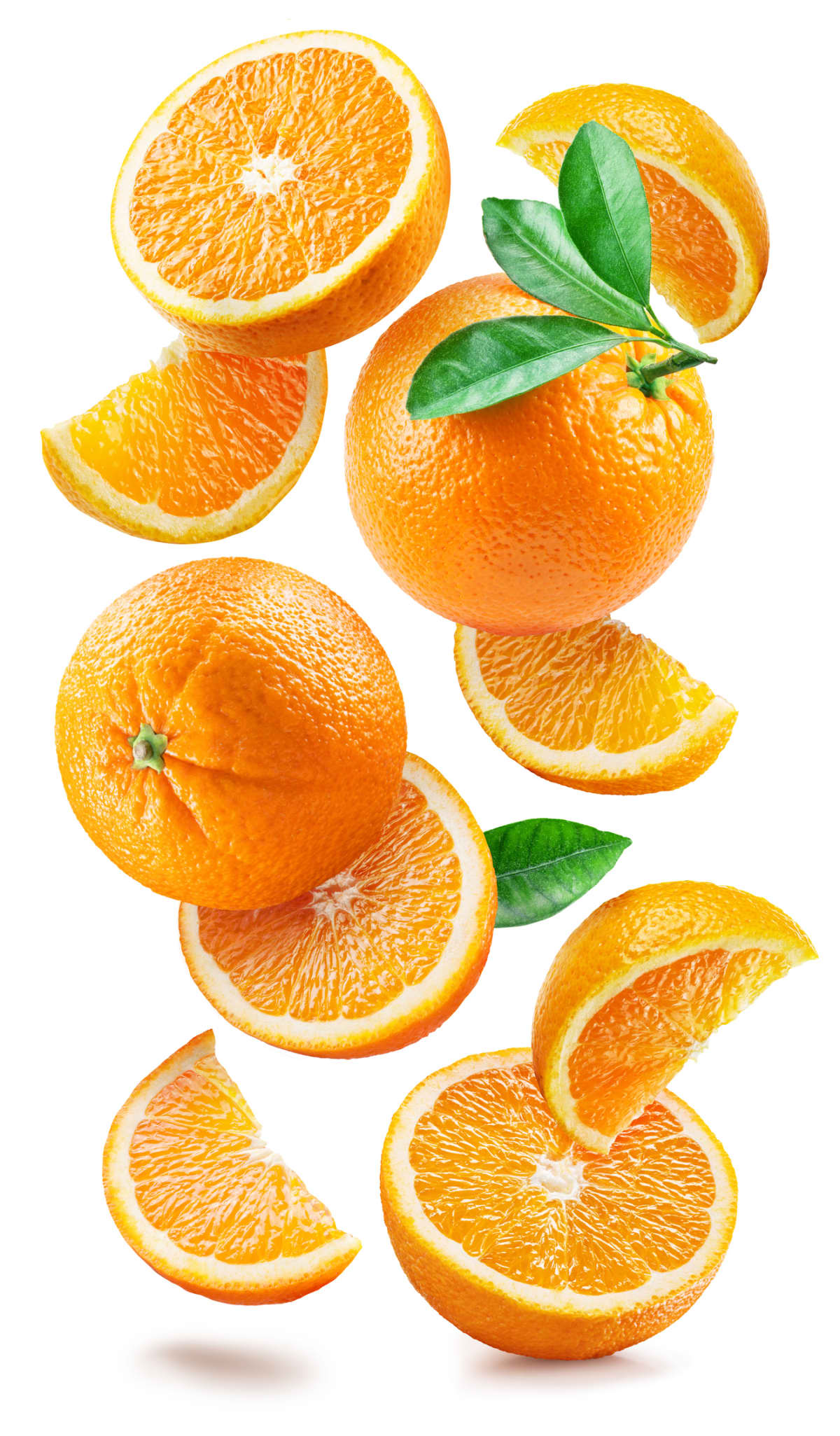 Ripe oranges with halves and slices with orange tree leaves randomly falling or levitating on a white background