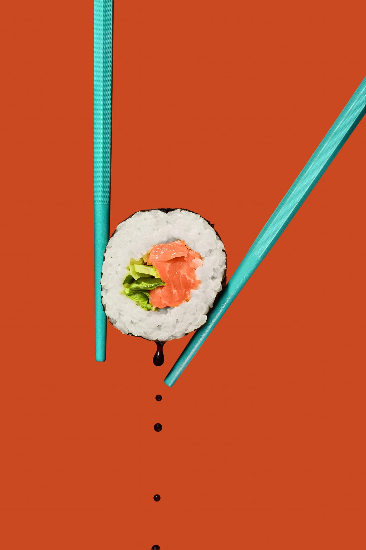 Sushi futomaki rolls with sushi, lettuce and spring onion, held with bright blue chopsticks against and orange background
