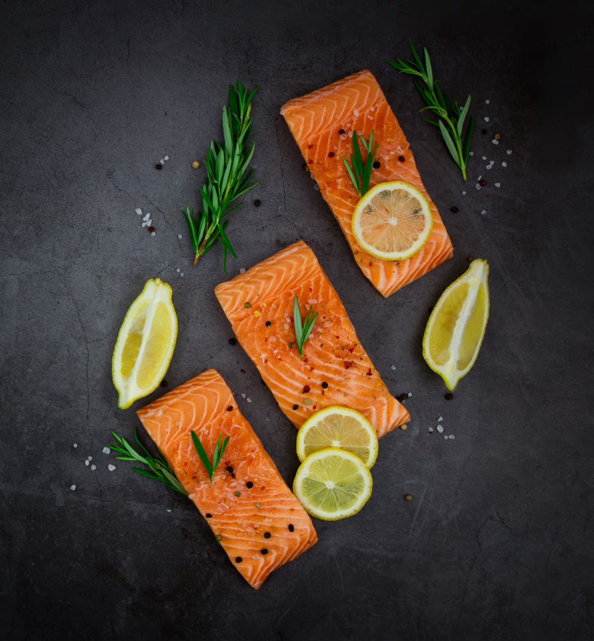 Salmon fillet steaks with lemon and herbs on a black background.