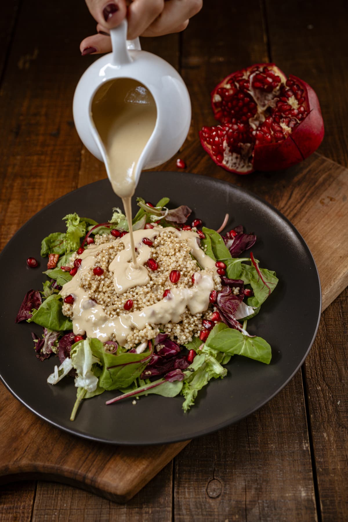 Vegan salad with millet and pomegranate with tahini dressing being poured onto it