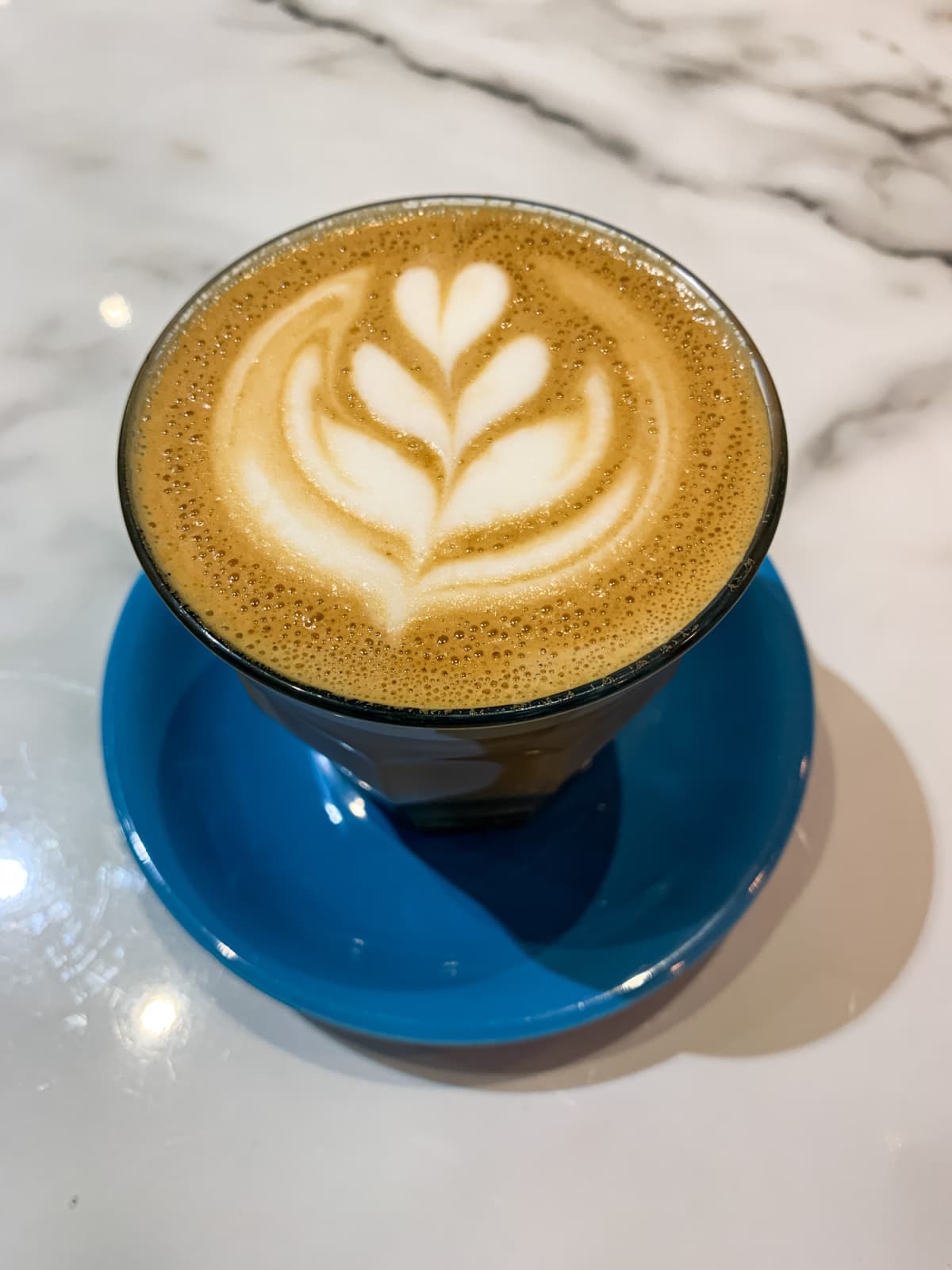Mug of flat white coffee on a white marble background with heart flower shape latte art