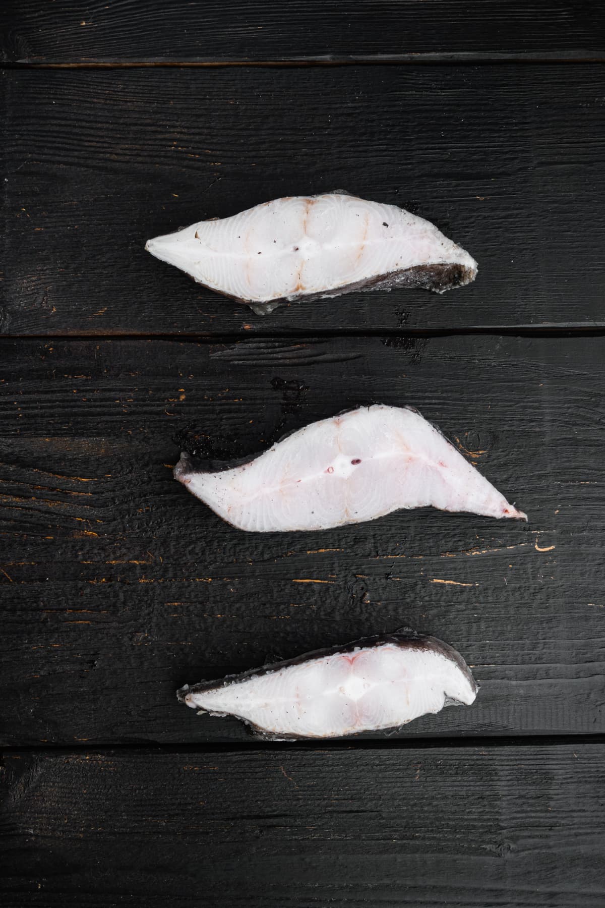 Frozen fish cut set, on black wooden table background, top view flat lay