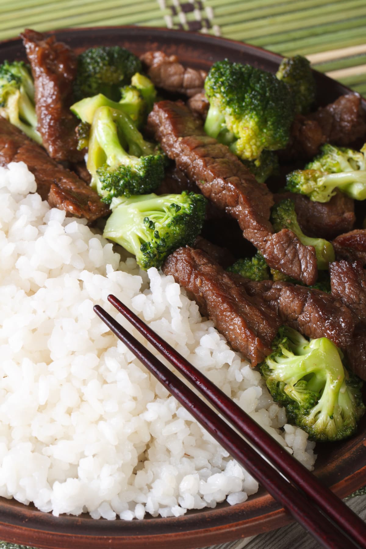 Pieces of beef with broccoli and rice on a plate with chopsticks