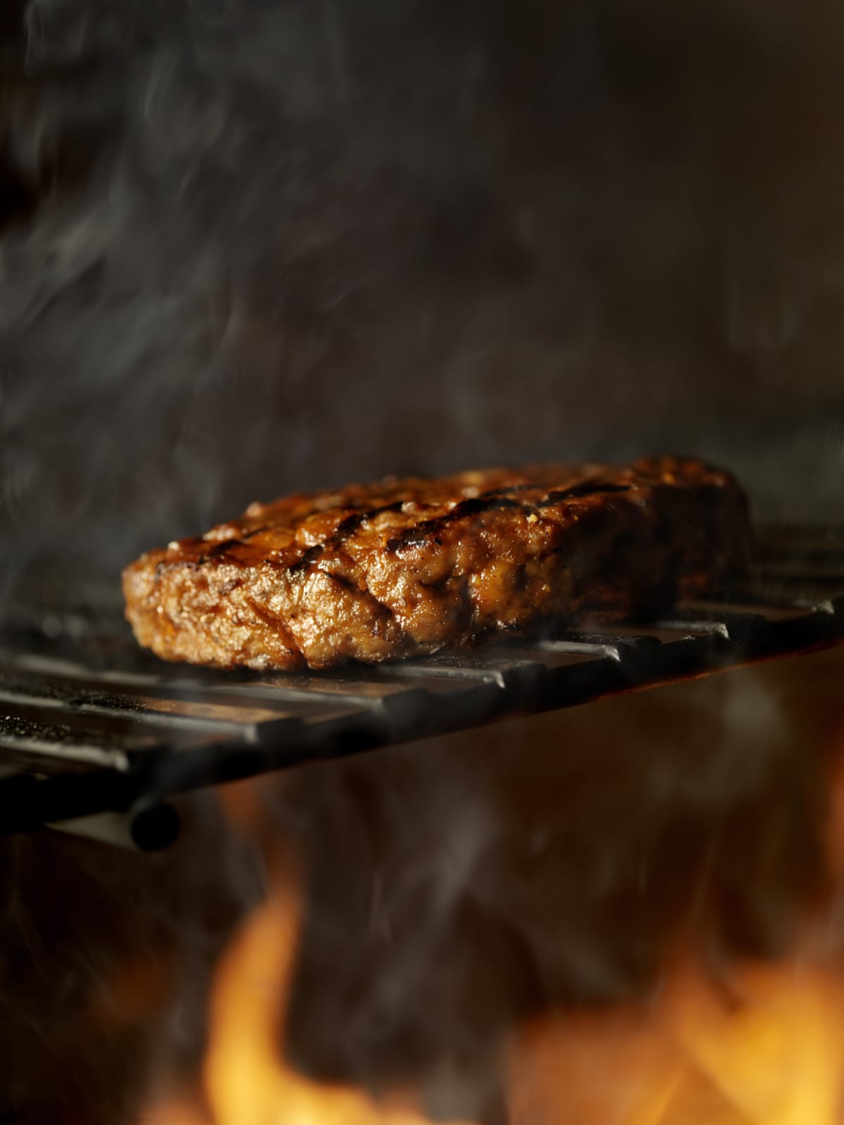 Burger being grilled on grill with smoke rising