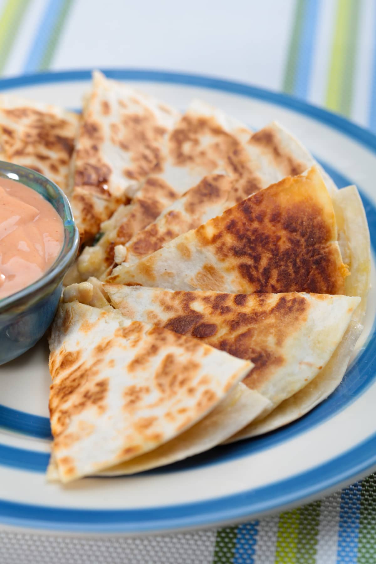 Sliced quesadilla on plate with bowl of sauce