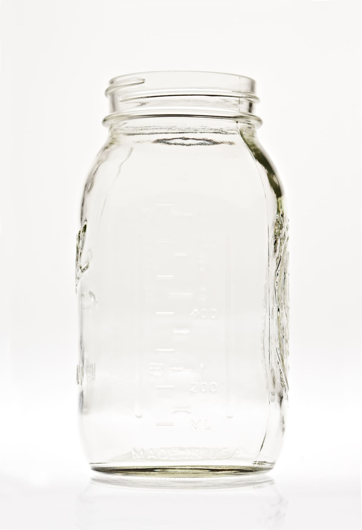 An extreme close up vertical photograph of an isolated in white empty clear glass canning jar.