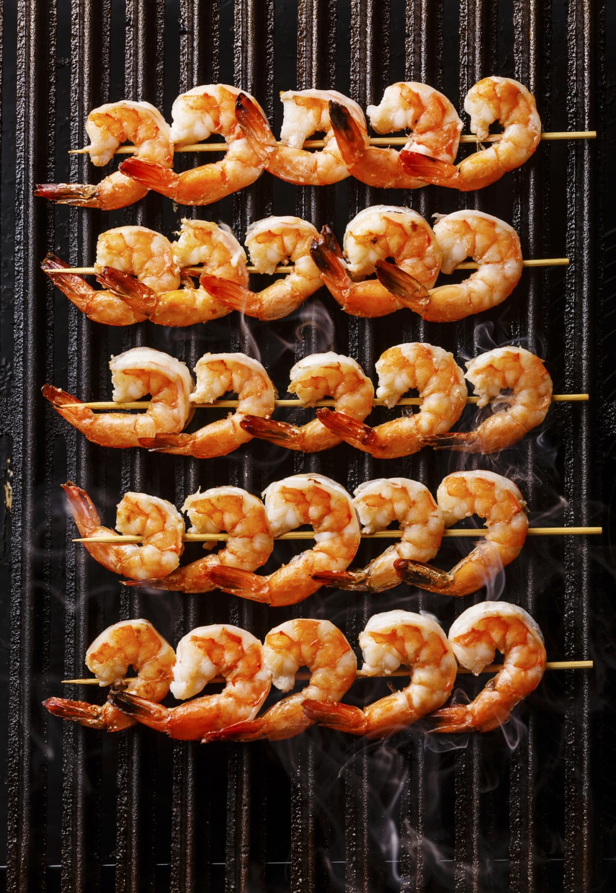 Grilled fried Prawns on skewers on black cast iron grill background