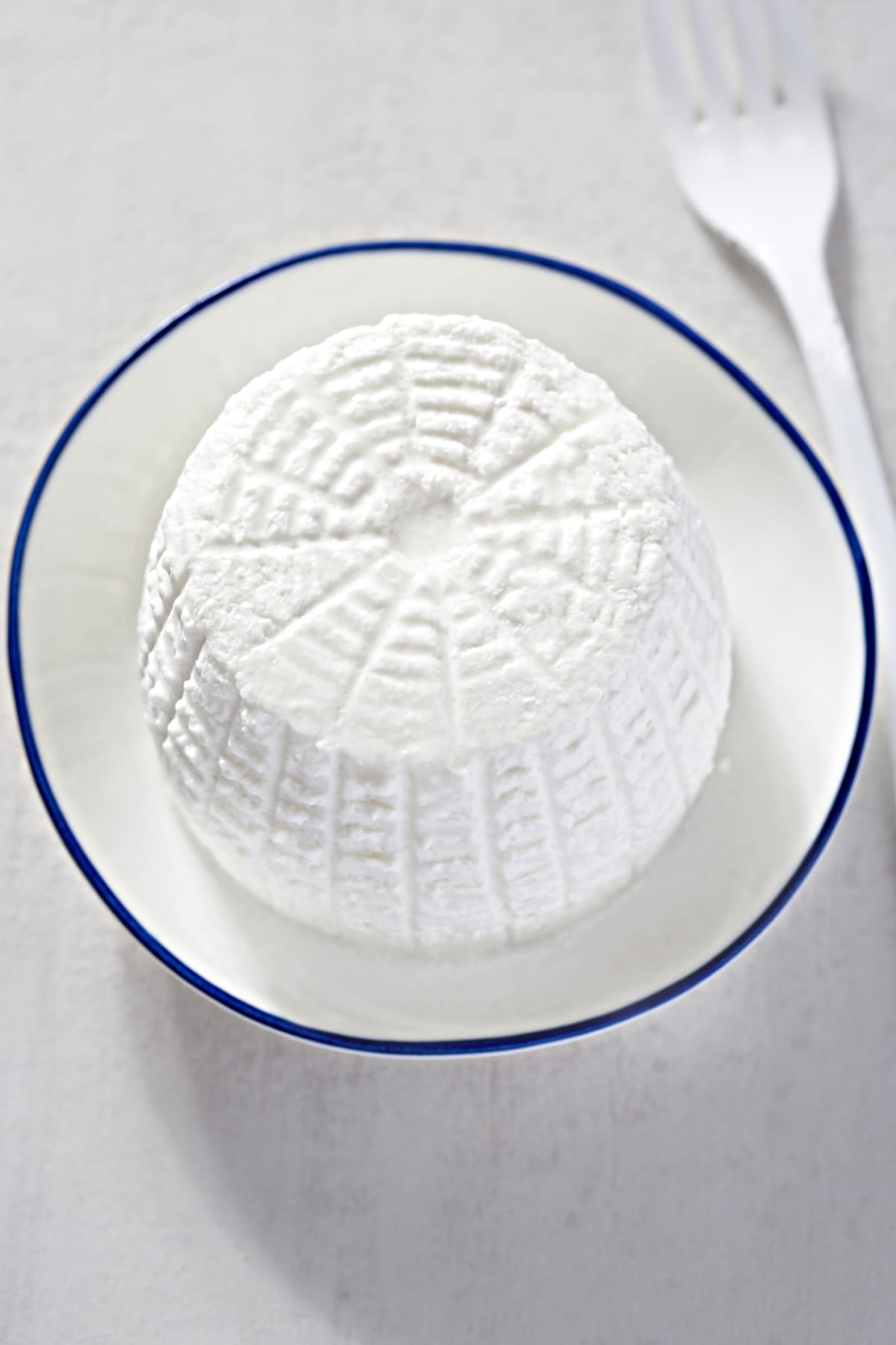Ricotta cheese on white plate with blue rim next to fork