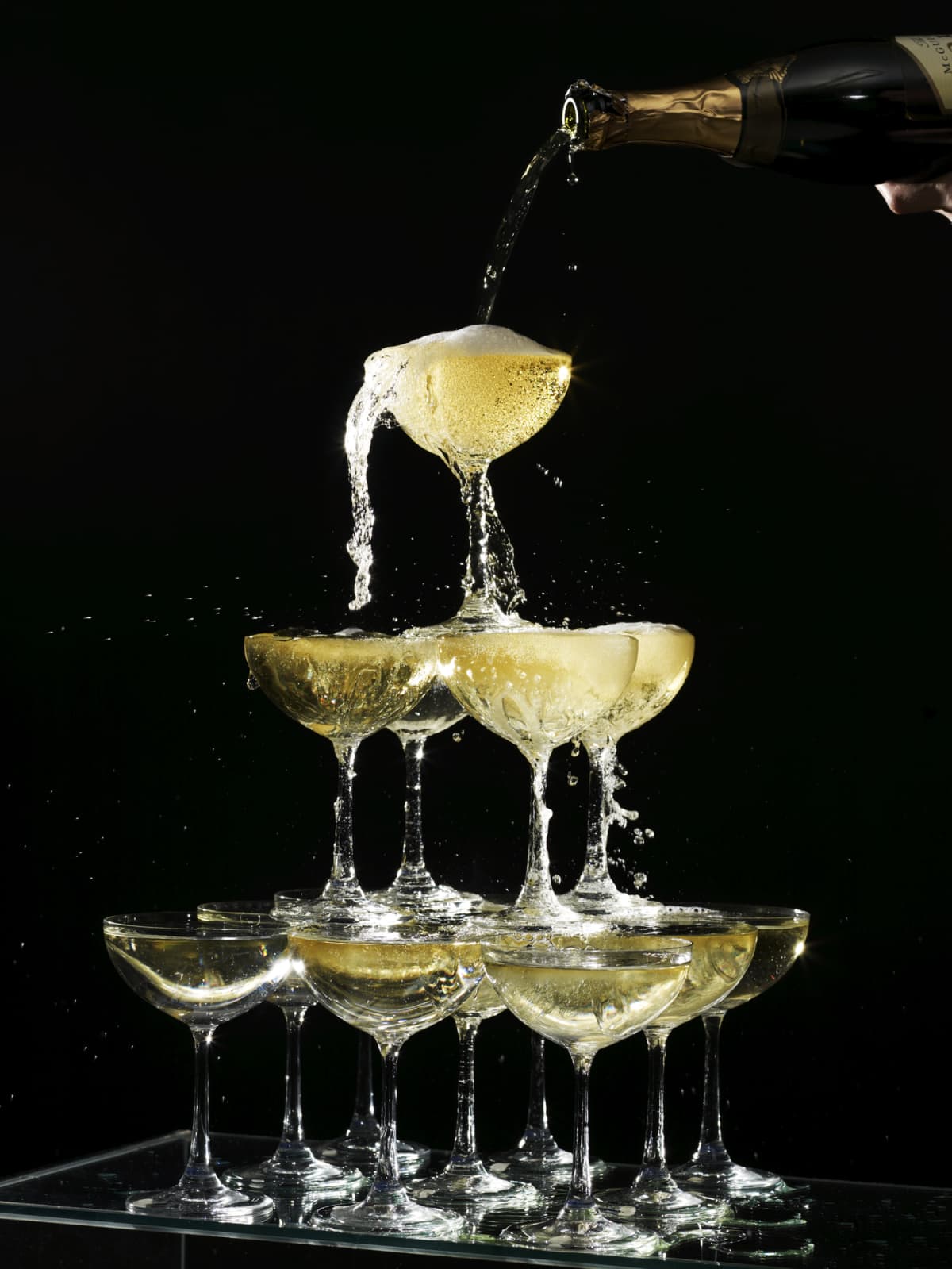 Glasses of alcohol stacked into tower on one another with alcohol pouring into top glass