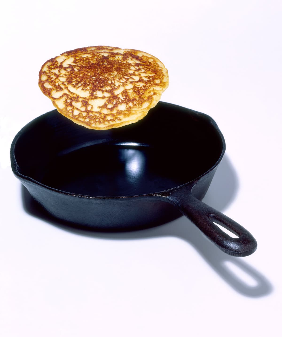 Pancake being flipped above pan on white background