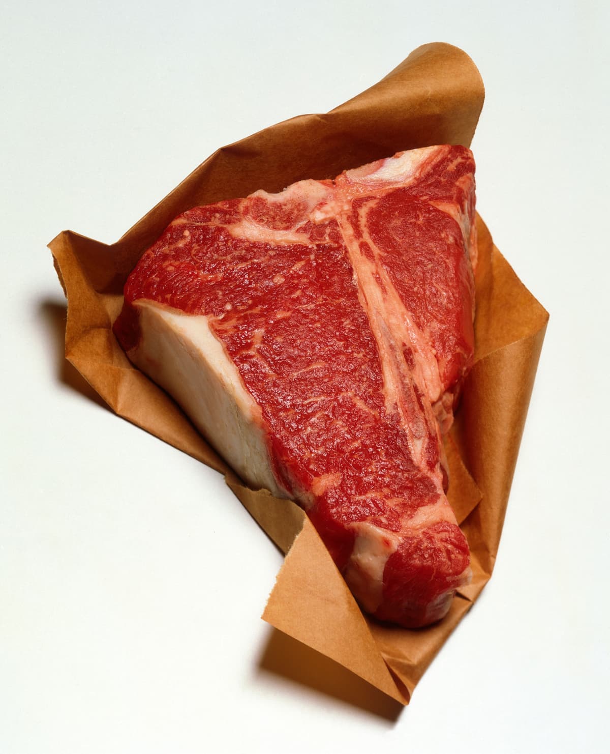 Raw T-bone steak on brown paper.