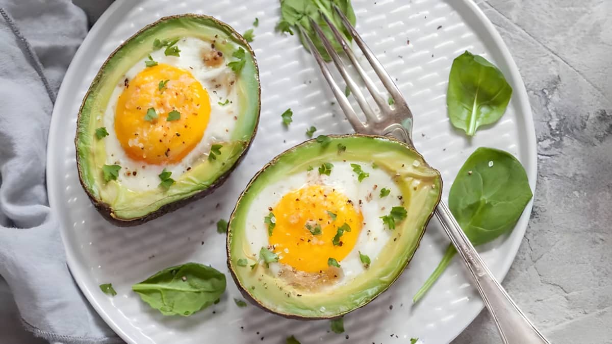 Egg avocado boats on white plate with green herbs