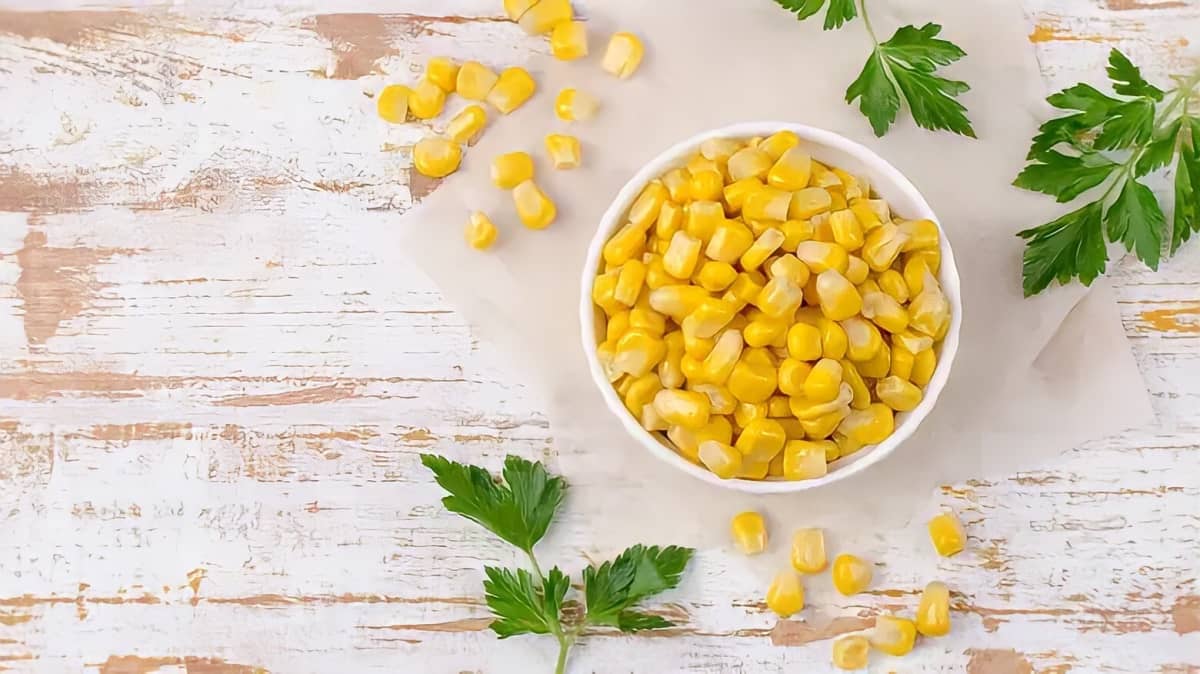 Canned corn in a white bowl on a white surface with herbs and more corn