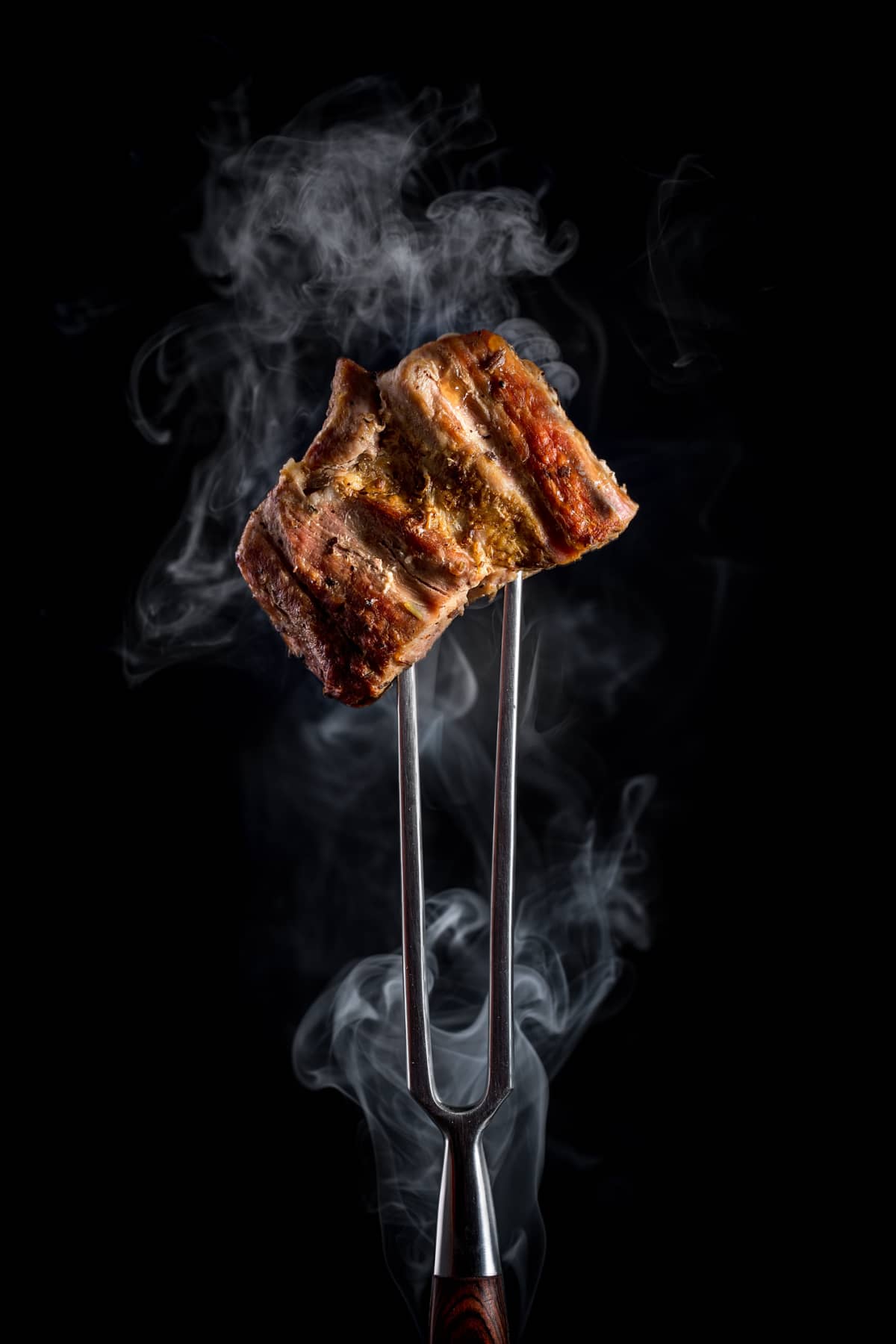 A fork holding barbecued meat on black background