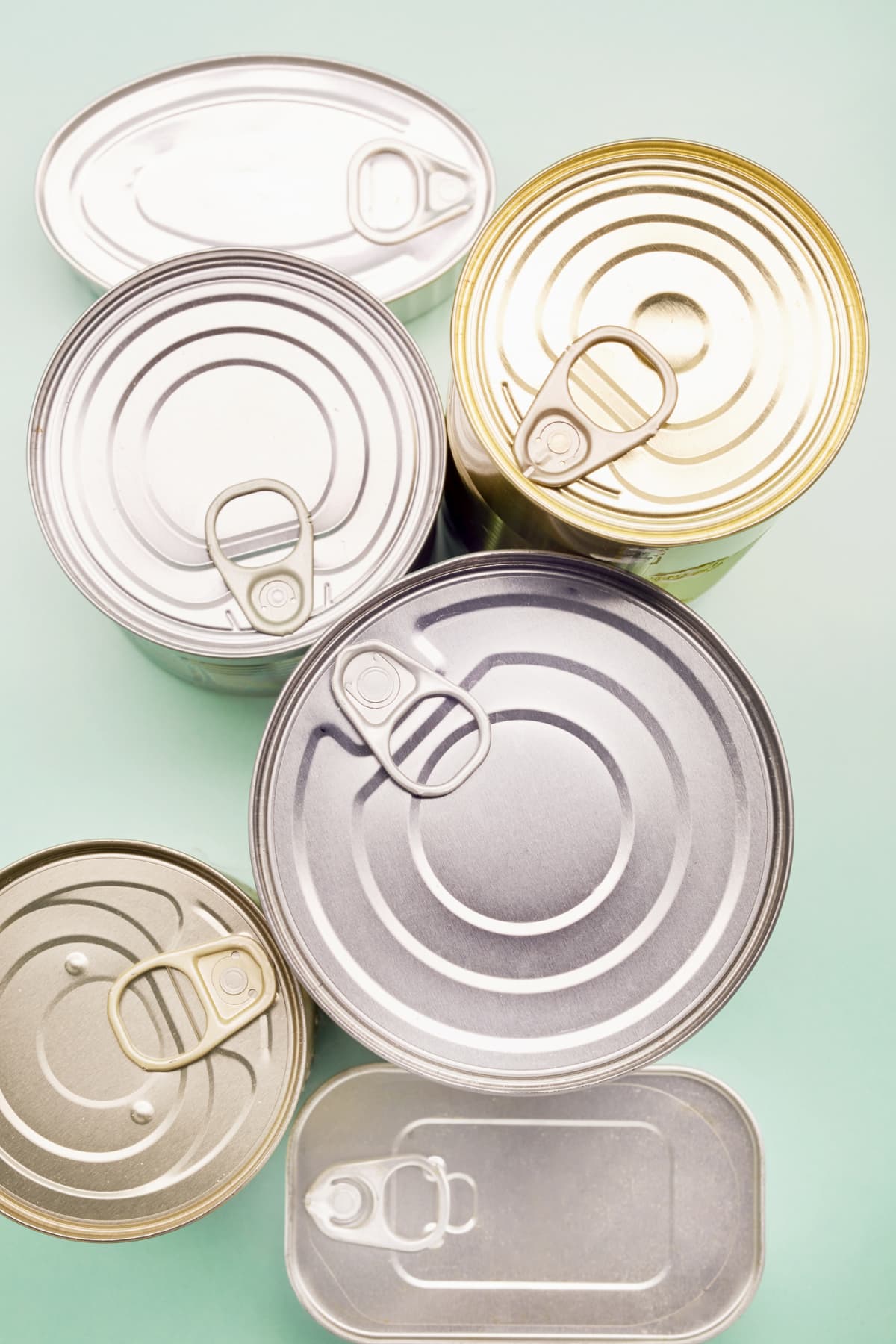 Cans with pull tabs next to each other on teal surface